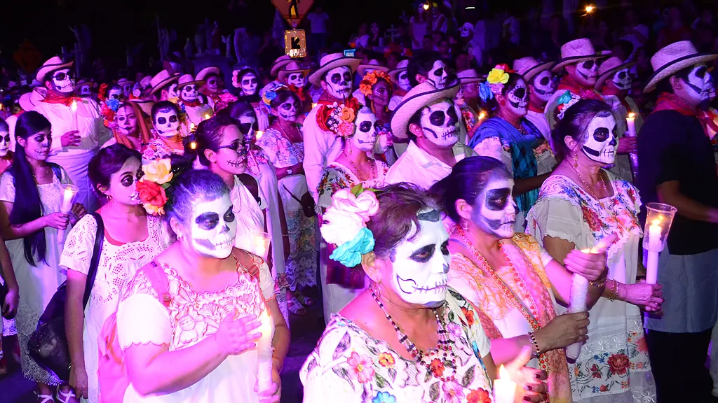 Personas con maquillaje de calavera, ropa yucateca y velas en la mano caminan juntas durante el Paseo de las Ánimas en Mérida (foto de 2019).